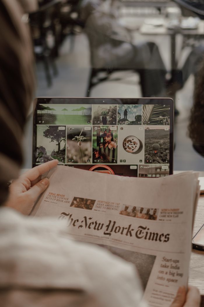 about-us-02 Woman reading The New York Times with a laptop displaying images in a café setting.